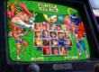 Um close técnico de um monitor CRT em um gabinete de arcade, exibindo a tela de seleção de personagens de Street Fighter Zero 2